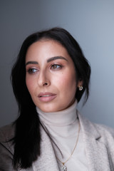 Portrait of a smiling mid-aged business woman in a light milk-colored trouser suit and turtleneck against a light wall.