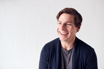 Portrait Of Casually Dressed Smiling Man Standing Against White Studio Wall