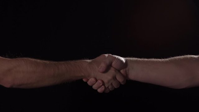 Caucasian males firmly shake hands on black background, close up isolated, 4K
