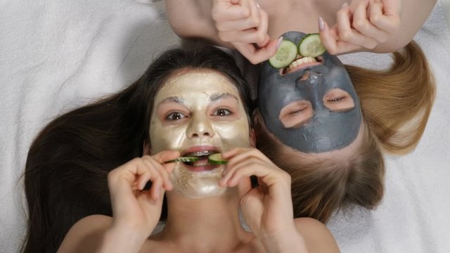 Smiling female bst friends having fun with sliced cucumber while applying clay face mask, isolated shot on white background at beauty salon. Spa time at bridal shower. Top view. 4k