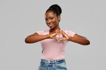love and valentine's day concept - happy smiling african american young woman making hand heart...