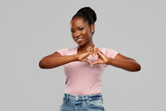 love and valentine's day concept - happy smiling african american young woman making hand heart gesture over grey background
