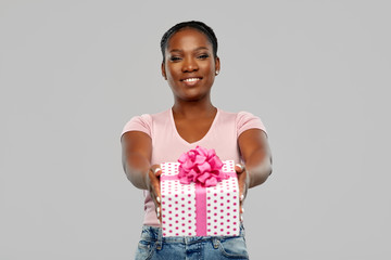 birthday present and people concept - happy african american young woman with gift box over pink background