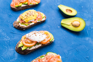 Sandwiches with smoked salmon, eggs, sauce and avocado on blue background. Concept of breakfast and healthy nutrition.