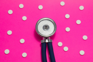 Head of stethoscope is on pink background surrounded by pills or tablets with ornament of polka...