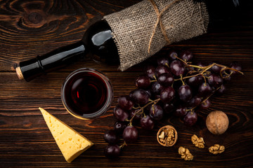 Red wine, grape, cheese and walnut on dark wooden background.