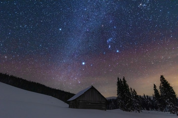 A bright starry night in the mountains with the Milky Way in the sky, Venus and millions of stars highlighting beautiful mountain huts in the valley.