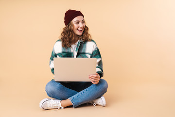 Photo of happy woman smiling and using laptop while sitting on floor