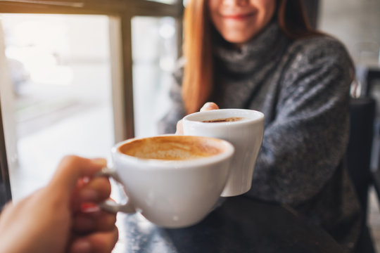 Closeup image of a woman and a man clinking coffee mugs in cafe