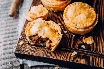 Fresh Traditional Australian meat mini pie on the wooden board on table background, closeup with copy space, rustic style