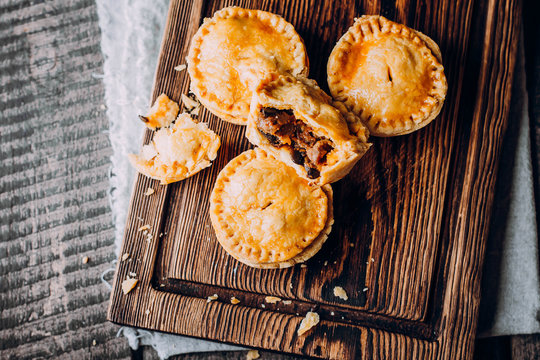 Fresh Traditional Australian meat mini pie on the wooden board on table background, closeup with copy space, rustic style