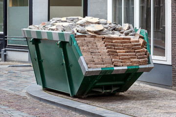 Neat industrial skip parked on the clean sidewalk full loaded with bricks and rubble in Dordrecht in the Netherlands