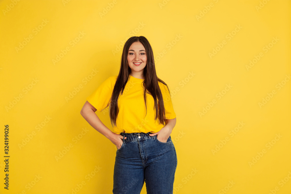 Wall mural Smiling, posing. Caucasian woman's portrait isolated on yellow studio background. Beautiful female brunette model in casual style. Concept of human emotions, facial expression, sales, ad, copyspace. - Wall murals