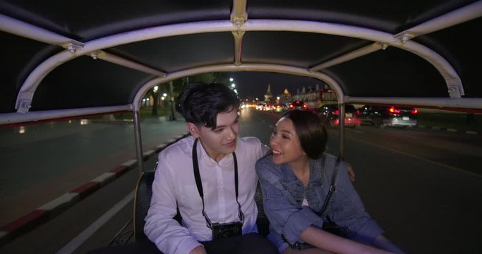 Asian couple travelling inside a Tuk Tuk vehicle in the street at Bangkok city night time. Sweet couple travel in holiday trip.