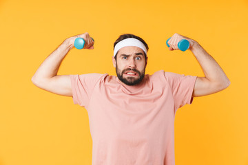 Fototapeta premium Image of muscular athletic young man having fun and lifting dumbbells