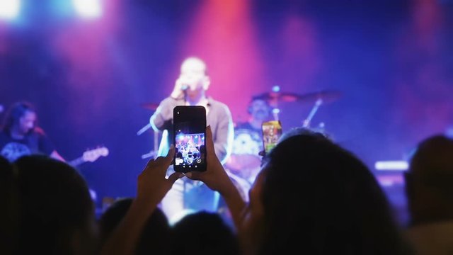 Silhouettes of concert crowd in front of bright stage lights. Hands with phones sticking out of a crowd during a concert. A large group of people at concert.