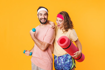 Portrait of athletic young couple holding dumbbells and fitness mat