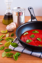 Sartén con tomate frito y hojas de albahaca sobre tabla de madera