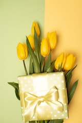 Yellow, fresh tulips in a vase on a wooden table and a gift.