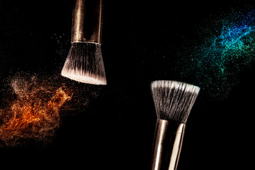 Two make up brushes with flying color powder, product on black background. Concept of glamour make...