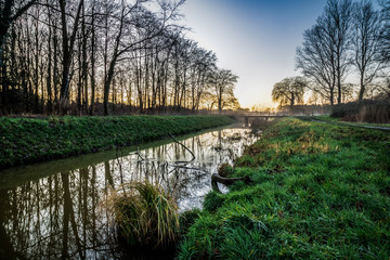 A canal runs through a meadow landscape during the sunset in the Netherlands