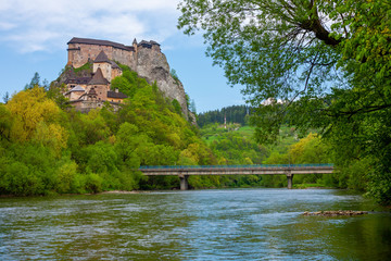 Fototapeta na wymiar The picturesque Orava castle on top of a cliff with autumn forest and river with bridge in the foreground in Slovakia