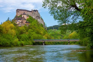 Fototapeta premium The picturesque Orava castle on top of a cliff with autumn forest and river with bridge in the foreground in Slovakia