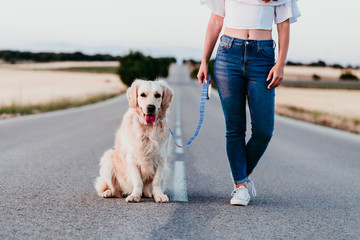 young woman walking by the road with her golden retriever dog at sunset. Pets outdoors