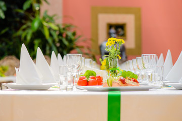 Long served table with plates, glasses, napkins, chairs and dishes