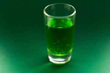 A green drink in a transparent glass stands on a green background. Carbonated liquid in a shot glass. Drink in a glass
