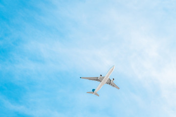 Fototapeta na wymiar Large commercial passenger airplane flying under blue sky viewed from below