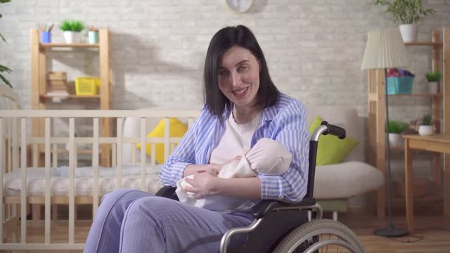 portrait of a young disabled woman and a newborn looking at the camera and smiling