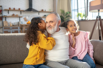 Cute long-haired girl telling something on the ear to her granddad