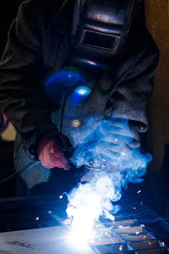 worker in protective uniform and mask welding metal. man using electric welding machine