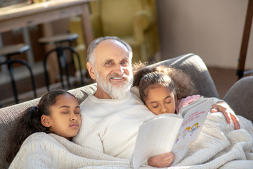 Two girls sleeping on the sofa hugging their granddad.