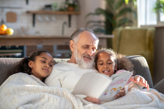 Grey-haired Granddad Reading Bedtime Stories To His Granddaughters