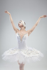 Close up of graceful classic ballerina dancing on white studio background. Woman in tender clothes like a white swan. The grace, artist, movement, action and motion concept. Looks weightless.