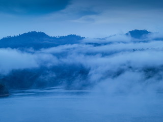 view of soft mist moving on top hill with mountain and cloudy sky background, Khao Sok National Park, Surat Thani, southern Thailand.