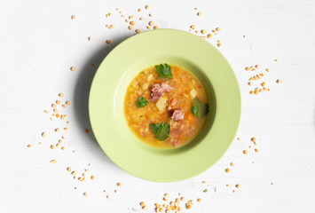 Soup with split peas, smoked meats, potato, parsley in green plate on white concrete background