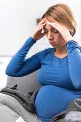 Pregnant tired exhausted woman with stomach and head issues at home on a couch, being sick.