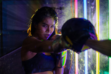 Beautiful 20s Asian Woman trains punching with coach on Silver gold Mitts Gloves. Office Girl exercise at Modern multi color Fashion Neon Muay Thai Boxing Gym with sweat water splash reflect light