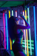 Beautiful 20s Asian Woman finish training in sport bra. Office Girl drinks water from clear bottle through mouth in Modern multi color Fashion Neon Muay Thai Boxing Gym with sweat water splash