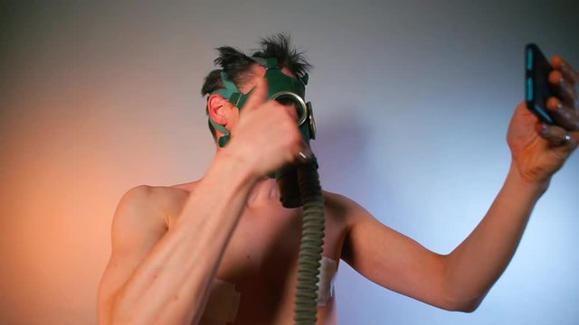 A male video blogger in a gas mask makes video at a party. Tells, gesticulates. Kinky people concept.