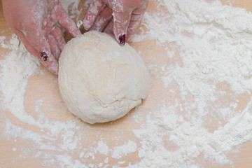 Kneading dough with flour on a wooden table at home