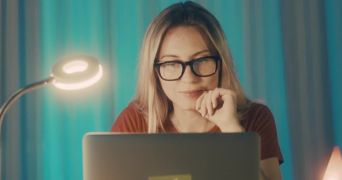 Close-up portrait caucasian business woman with eye glasses smiling and using computer in home workspace. 4K slow motion.