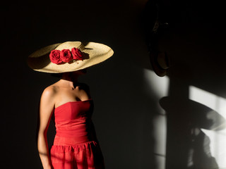 Joven con vestido rojo y sombrero de paja con flores rojas y sombra en la pared