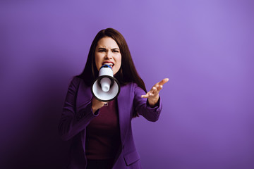 irritated young woman screaming in megaphone while showing indignation gesture on purple background