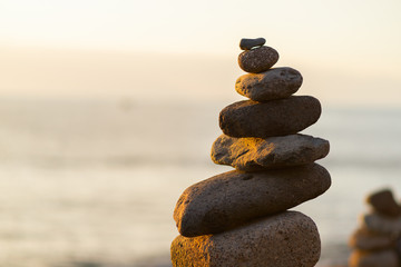 Balanced stone pyramide on shore of the ocean at dawn. Sea pebbles tower closeup symbolizing stability, zen, harmony, balance.