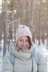 Obraz premium girl in winter clothes smiles and feeds the birds from the head in the park