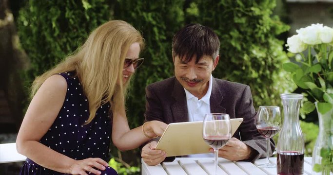 MS Senior Couple Sharing a Tablet to look at pictures and browse the internet while enjoying a glass of wine on Garden Patio. Senior Shot in R3D (6K RED RAW)